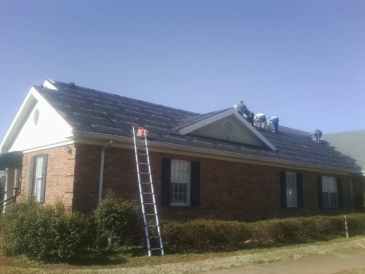 Crew tearing shingles off a brick ranch roof with a ladder set — Emergency Roof Repair work by our crew in Kennebunk