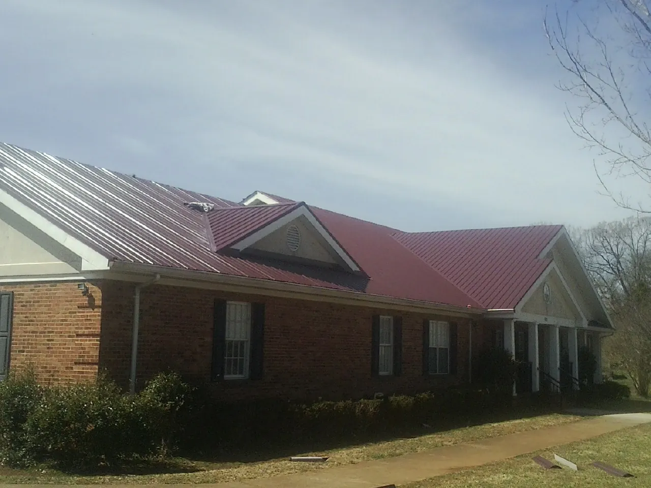 Red metal roof with gabled entries on a long brick building, from a Hail Damage Roof Repair job in Kennebunk
