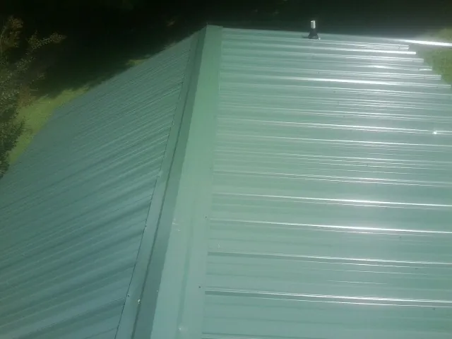 New green metal panels meeting at the ridge of a roof — Flat Roof Repair work by our crew in Kennebunk
