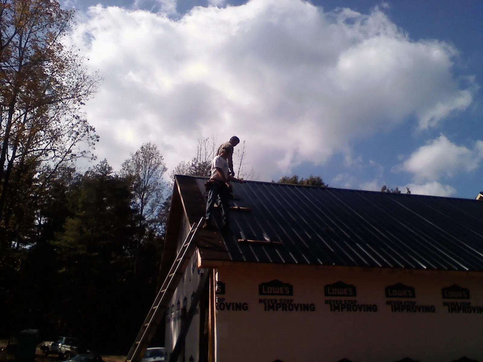 Roofer fastening dark metal panels high against a cloudy sky, from a Roof Inspection job in Kennebunk