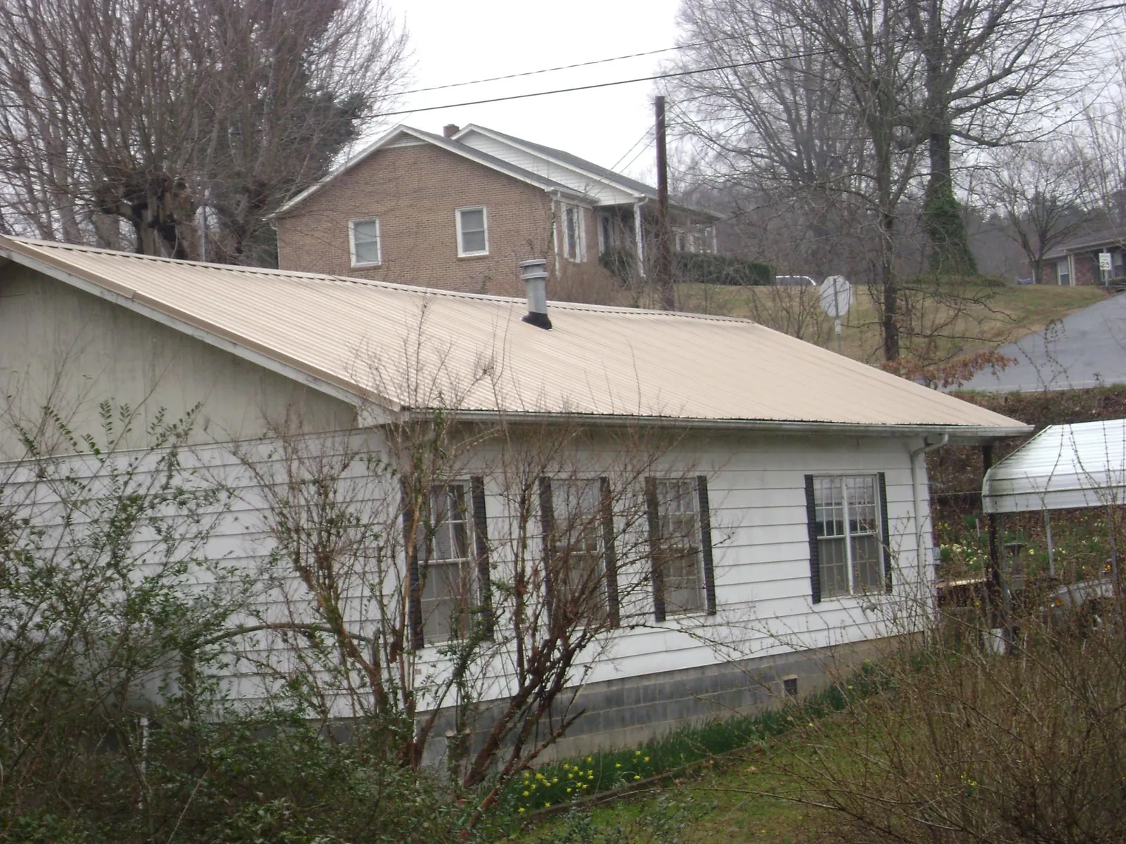 Tan metal roof on a white sided house set into a hillside — Commercial Roofing by Roofing Brothers in Kennebunk